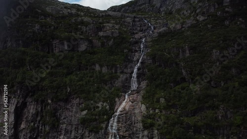 High waterfall flows into a lake in norway on a cloudy day with sun rays