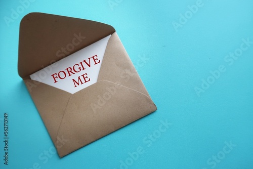 Card in craft envelope on blue copy space background with text written FORGIVE ME, to ask someone to forgive, to say sorry or apologize for mistake making photo