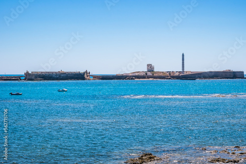 Rocks and boats in the turquoise sea and San Sebastian castle and fortress on the horizon, Cádiz SPAIN