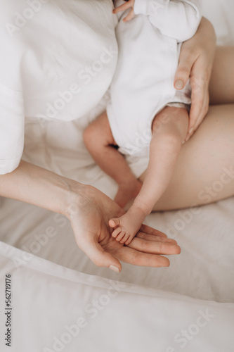 mother gently touches the legs of a newborn baby lying on a white bed close-up, motherhood, child care, caring parents