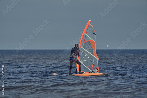 Mature woman windsurfer novice wants to raise the sail of a sailboard and continue surfing on a sunny autumn day.