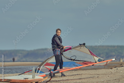 A mature woman in a wetsuit, a windsurfer, carries a sail to a sailboard. Preparing for surfing.