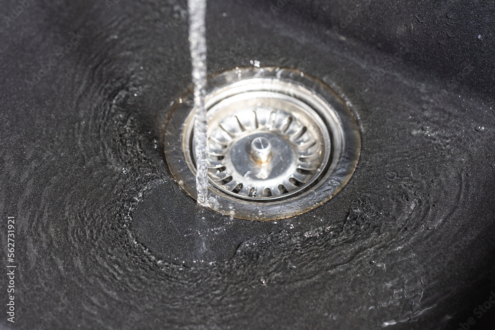 The water falling down from faucet to stainless sink and flow down to water hole, drink concept The water falling down from faucet to stainless sink and flow down to water hole, drink concept