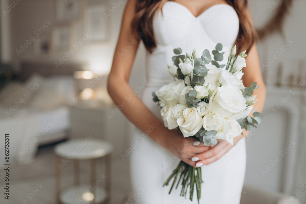 young girl in a white wedding dress holds in her hands a bouquet of flowers and greenery with a ribbon