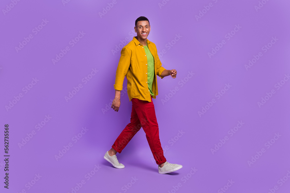 Full length profile portrait of satisfied friendly young man beaming smile walking isolated on purple color background Full length profile portrait of satisfied friendly young man beaming smile walking isolated on purple color background