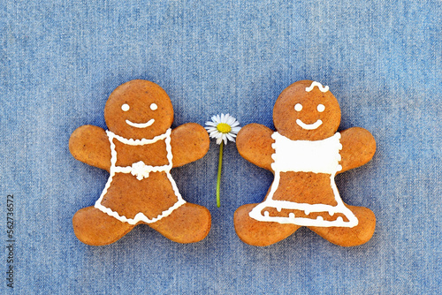 Cute smiling gingerbread couple with daisy flower on blue denim background