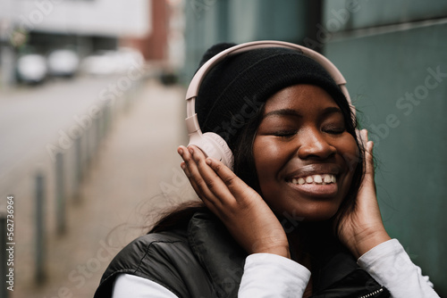 Positive afro woman listening music with headphones while standing outdoors