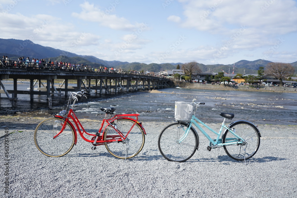 Red and light blue city bicycle parked beside the river with Kyoto Togetsu Bridge background