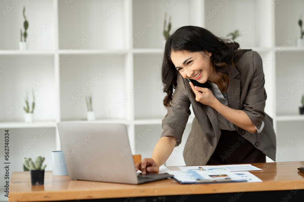 Smiling Asian businesswoman talking on the phone on modern business topics with satisfaction at her work and gesturing happily looking through information at her office. Smiling Asian businesswoman talking on the phone on modern business topics with satisfaction at her work and gesturing happily looking through information at her office.