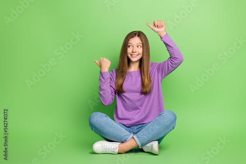 Full length photo of cheerful girl straight hairdo wear purple pullover look indicating empty space isolated on green color background