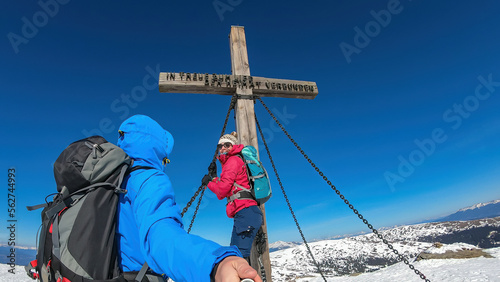 Couple reaching the summit cross of mountain peak Ladinger Spitz, Saualpe, Lavanttal Alps, border Styria Carinthia, Austria, Europe. Trekking in Austrian Alps in winter. Ski touring, snow shoe tourism