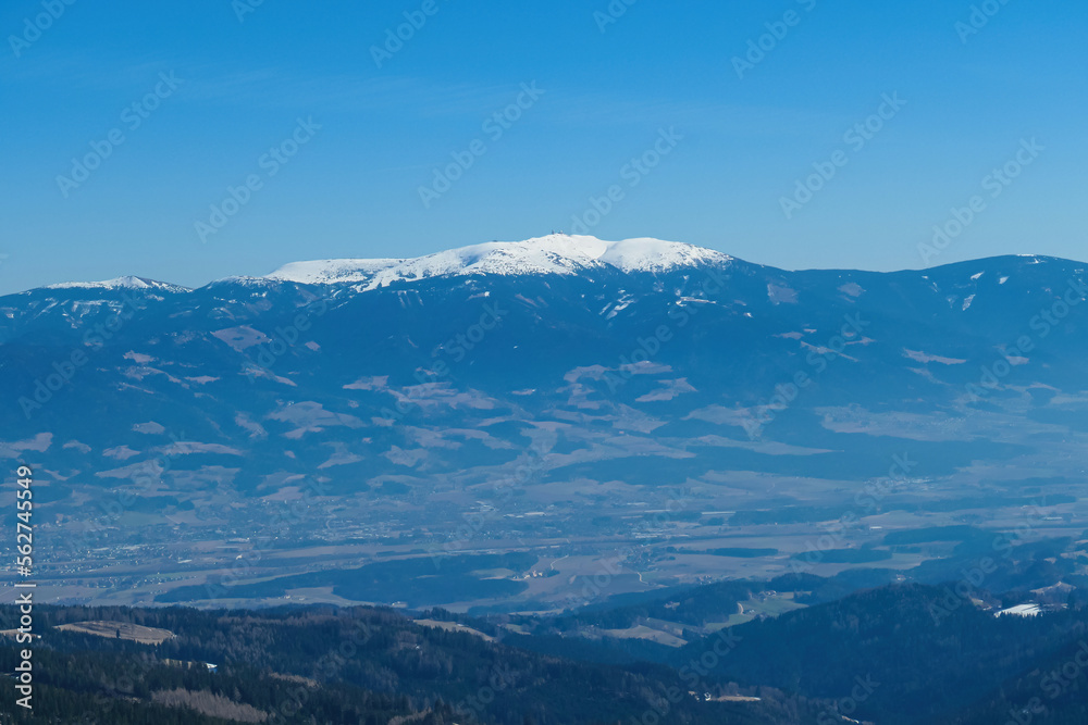 Panoramic view on the snow capped mountains of Koralpe seen from the mountain hut Wolfsbergerhuette (Wolfsberger Huette) on Saualpe, Lavanttal Alps, Carinthia, Austria, Europe. Valley in Wolfsberg Panoramic view on the snow capped mountains of Koralpe seen from the mountain hut Wolfsbergerhuette (Wolfsberger Huette) on Saualpe, Lavanttal Alps, Carinthia, Austria, Europe. Valley in Wolfsberg