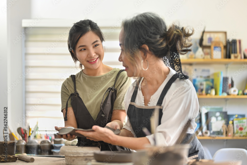 Fototapeta premium Earthenware workshop studio hobby or small business with Two diversity age of craftswomen shaping tableware from raw clay in workshop space.