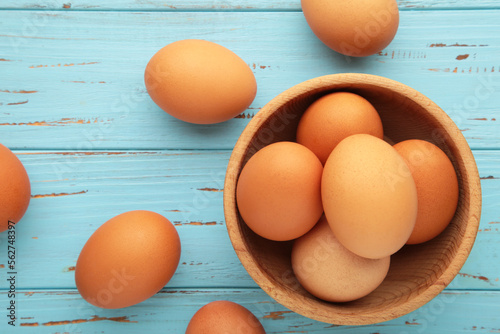 Top view of raw brown eggs on wooden bawl on blue wooden background. Eggs are a common ingredient in cooking.