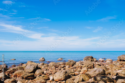 Rock on the coast in the smooth sea or ocean with clear cloud and blue bright sky background at the sandy beach on summer time