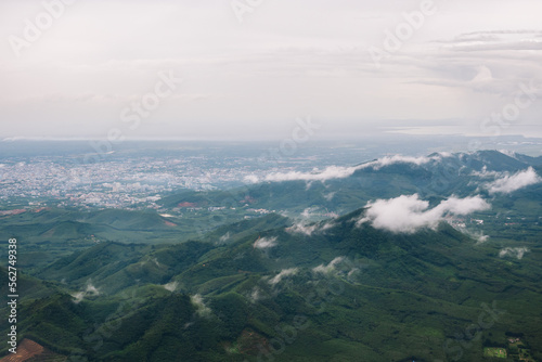 Aerial view from the top view of the forest, mountain, meadow and abundant plantation fields beside urban city, covered by white fluffy clouds