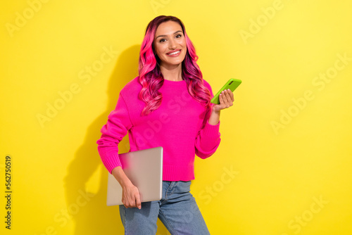Portrait of cheerful pretty lady hold netbook use telephone toothy smile isolated on yellow color background © deagreez