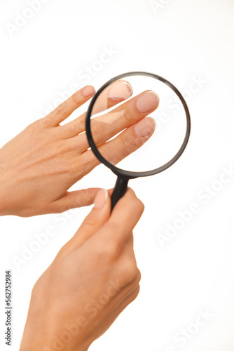 Close up vertical shot of a hand with french manicure under magnifying glass over white background.
