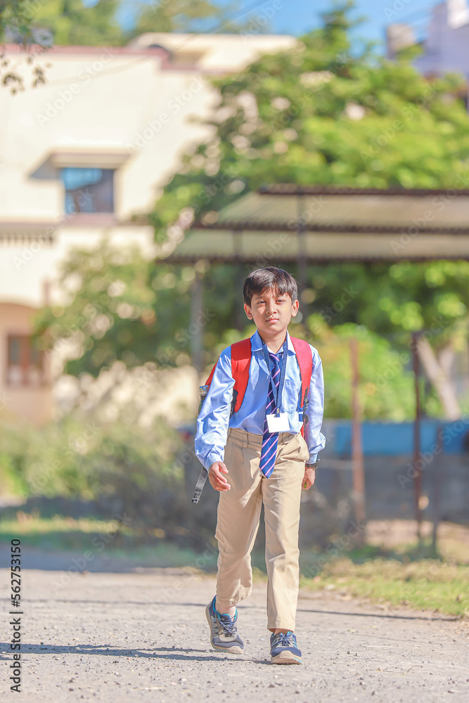 An Indian or asian little boy running on the road. Coming or going to school from home. Smiling kid.