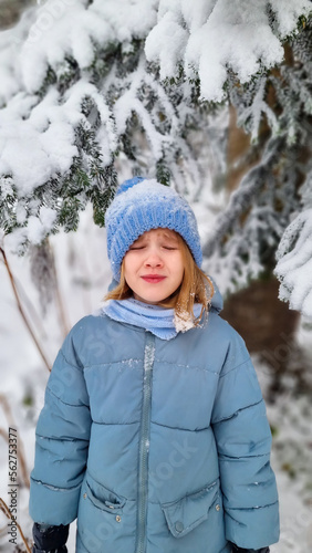 a sad cute girl in a blue coat under a snow-covered spruce. the beauty of winter nature, winter games and entertainment with children.