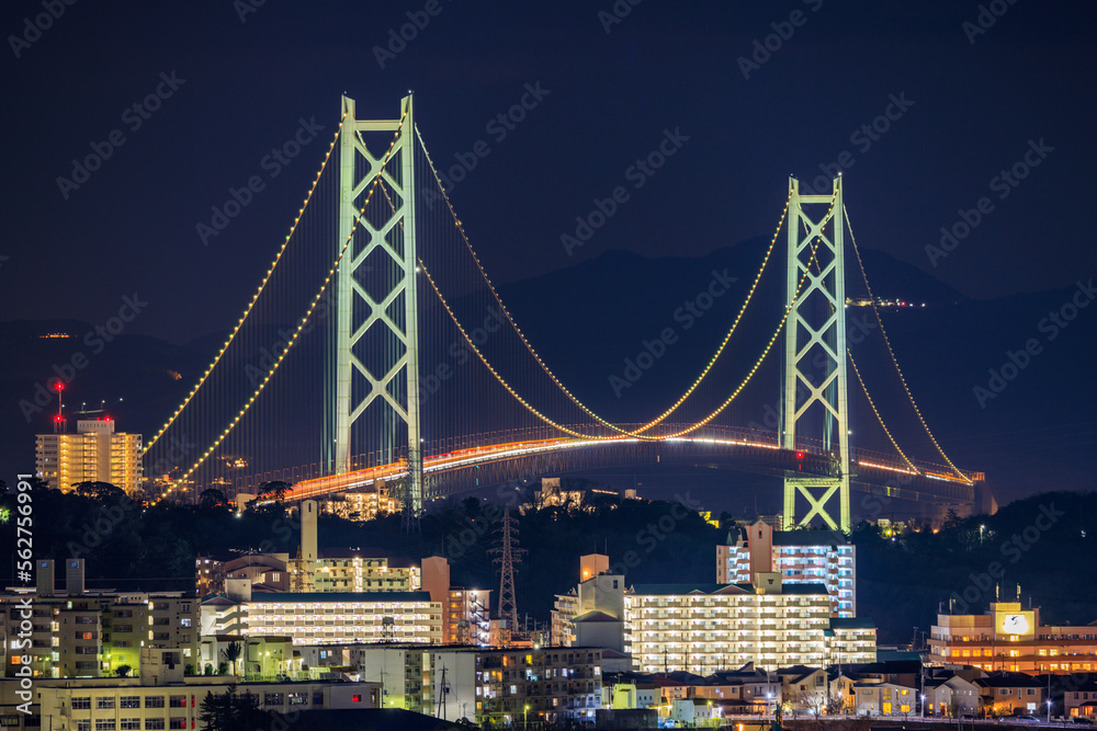 Obraz premium Illuminated Suspension Bridge Towers Over Apartment Buildings at Night