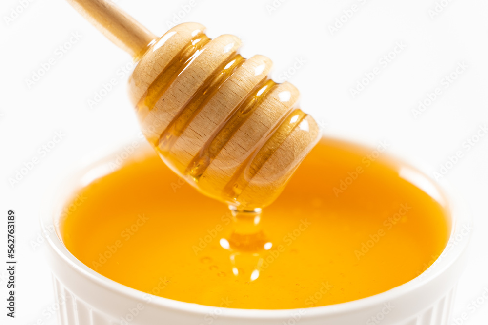 Liquid natural bee honey in a white ceramic bowl with a wooden spoon. Liquid natural bee honey in a white ceramic bowl with a wooden spoon.