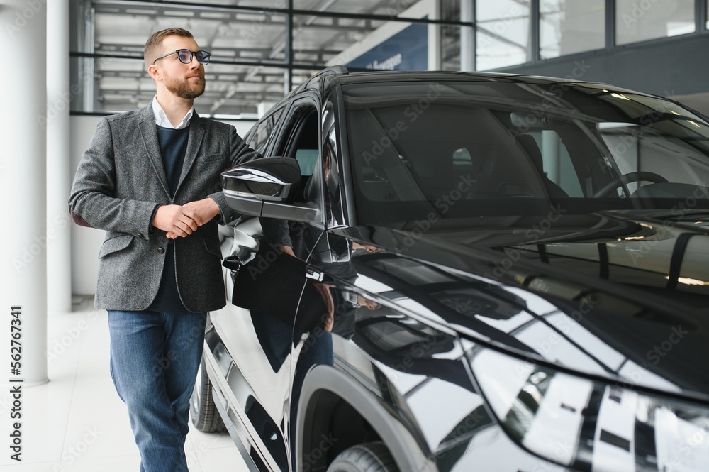 Making his choice. Horizontal portrait of a young man in a suit looking at the car and thinking if he should buy it Making his choice. Horizontal portrait of a young man in a suit looking at the car and thinking if he should buy it