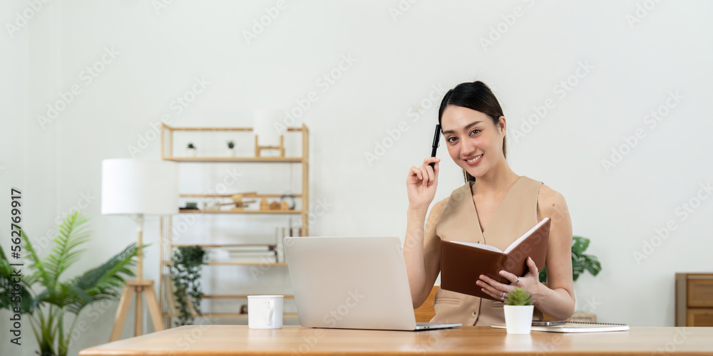 Happy Asian woman using laptop while taking note at home. Happy Asian woman using laptop while taking note at home.