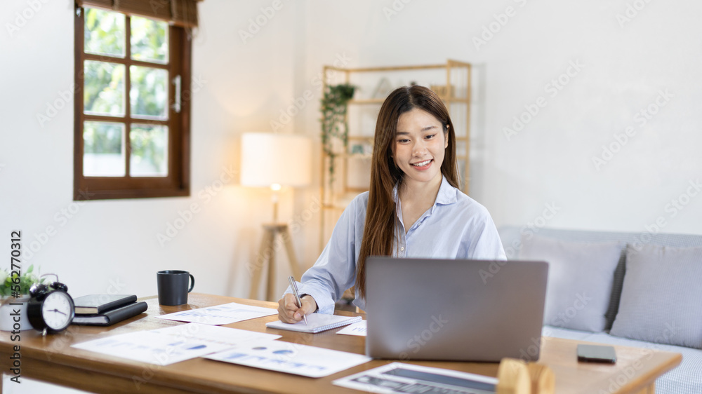 Beautiful young asian woman watching live video or video call of teacher teaching on laptop in her home, Take notes of important conversations and messages during the teacher's teaching. Beautiful young asian woman watching live video or video call of teacher teaching on laptop in her home, Take notes of important conversations and messages during the teacher's teaching.