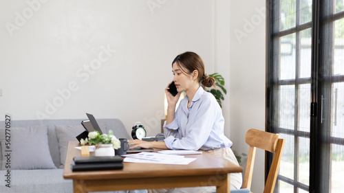 Woman working at home, Attractive woman chatting or talking with colleague on mobile phone at her home, Work for home, Remote conversation or meeting , Stay home, Use a cell phone or smartphone. © Puwasit Inyavileart
