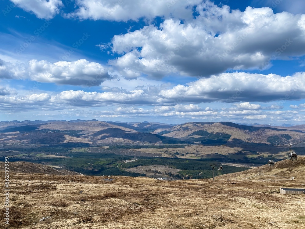 Scenic view of mountain peaks from Nevis Range Mountain Resort, popular hiking area. Blue sky with fluffy clouds. Scottish Highlands, Scotland, UK. Gondola on right.