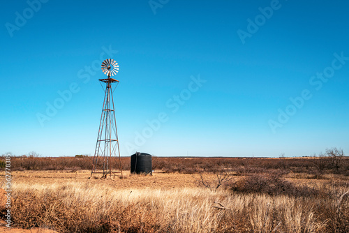 Rustic windmill, black water tank, and dried wildplants in the cattle pasture alongside rural road, Heartland of America wintry landscape in the Lone Star State of Texas, USA photo