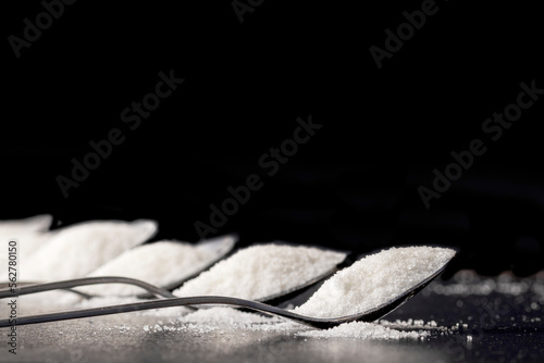 Tea spoon full of sugar crystals on a black background. Sugar substitutes concept. Selective focus.