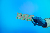 Mano con guante azul sujetando blister de pastillas sobre fondo azul.