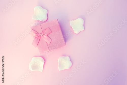 Pink gift box with ribbon and white petals on soft purple pink background 