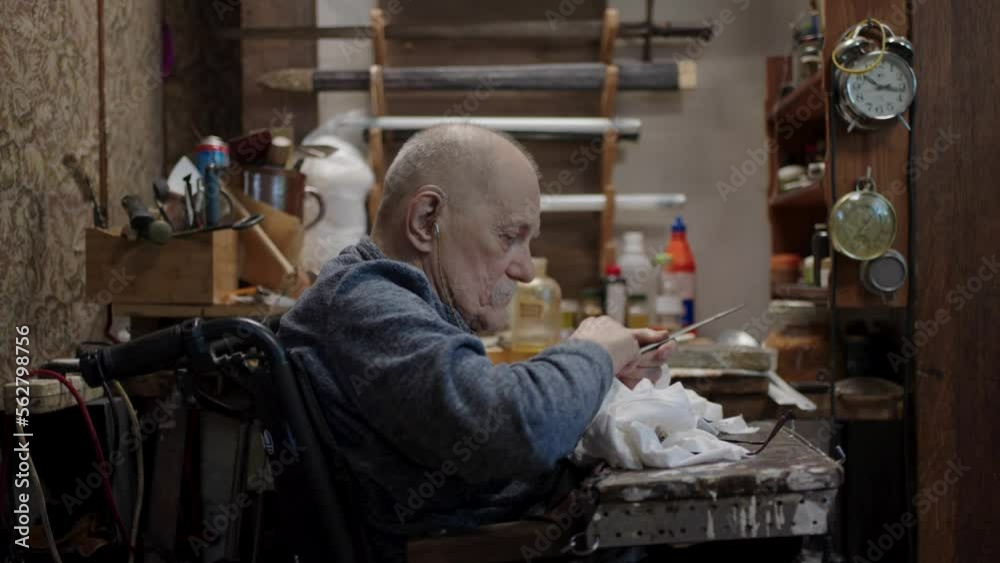 Senior gray haired male master in a wheelchair working at his workshop sharpening japanese swords blade Senior gray haired male master in a wheelchair working at his workshop sharpening japanese swords blade