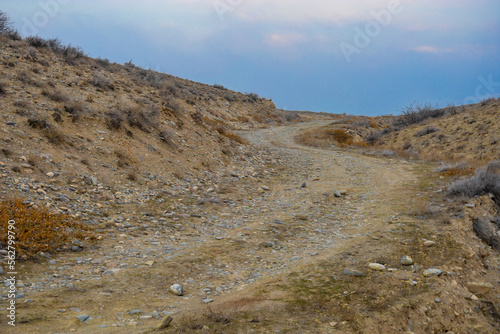 Obraz na płótnie Curved dirty ascending road covered by rocks in a treeless steppe