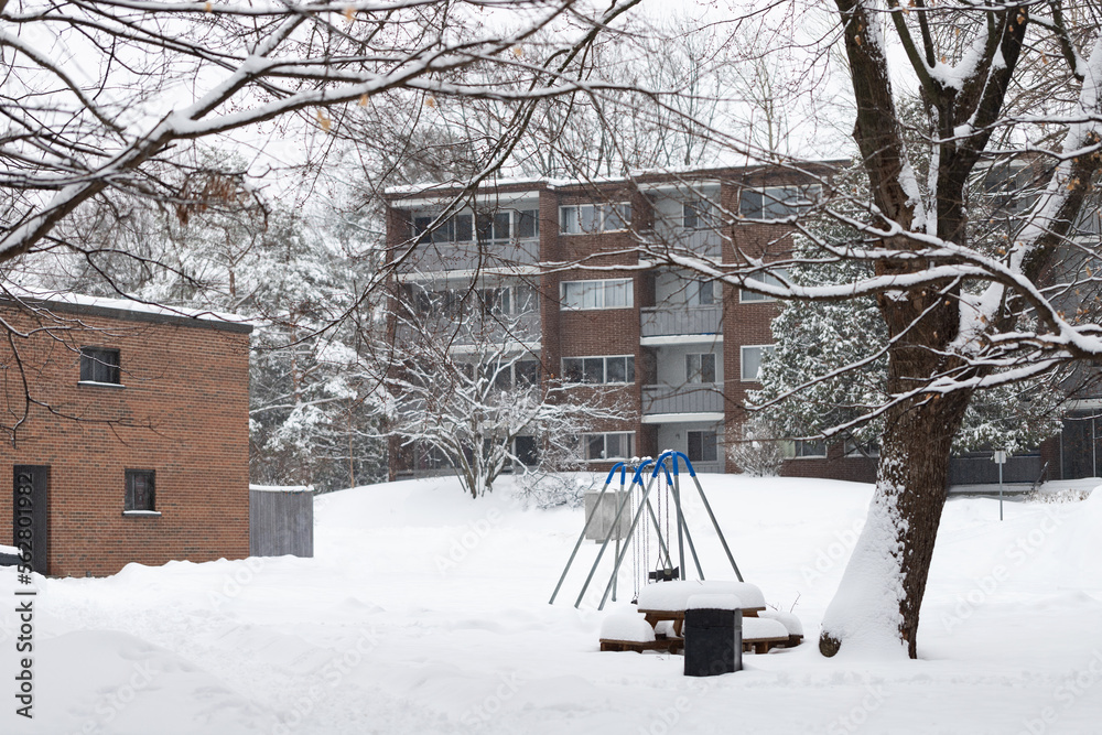 Winter snowy day in residential area near apartment building with playground outdoors. Neighborhood in cold weather covered with snow. Winter snowy day in residential area near apartment building with playground outdoors. Neighborhood in cold weather covered with snow.