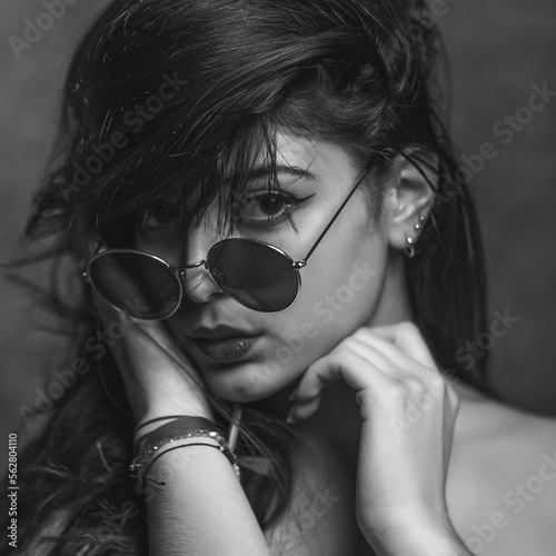 retrato primer plano de mujer morena y atractiva con gafas de sol redondas, blanco y negro sonre fondo gris en estudio