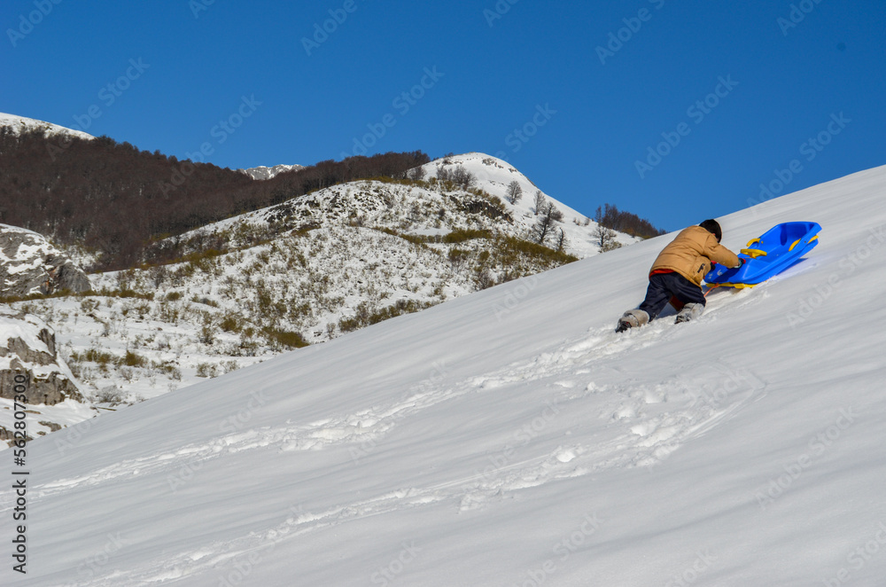 Niño empujando un trineo azul por una montaña