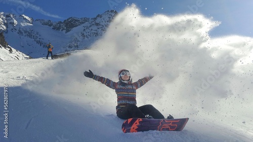 girl sitting on a slope in the val thorens ski resort is covered by a wave of snow produced by another skier
