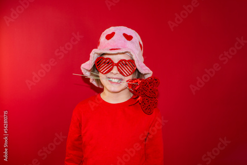happy boy in a pink hat with red hearts, in heart-shaped glasses, holds a heart