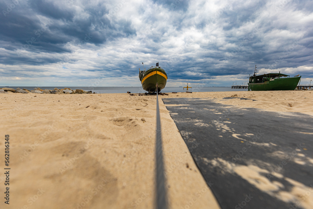 Obraz premium Long steel wire connected to small wooden ferry standing on a beach at cloudy day