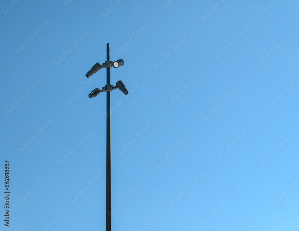 City surveillance cameras mounted on a tall metal pole. Blue sky in background, low angle view