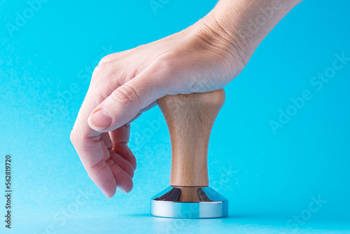 Hand and coffee tamper on a blue background. Close-up of hand with manual press for ground coffee