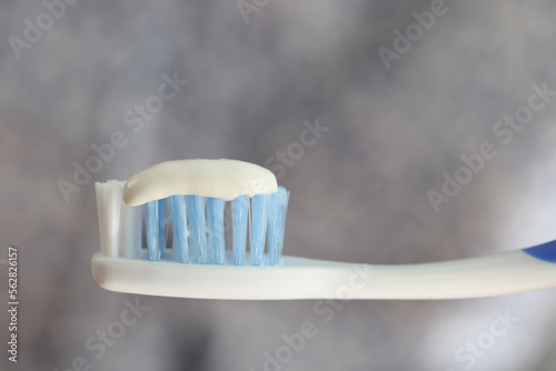 Toothbrush and toothpaste close up on gray blurred background.