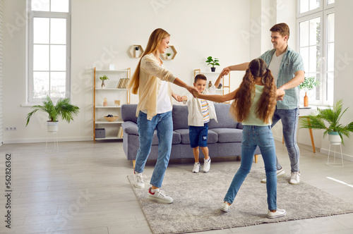 Happy family with two children are playing leading a round dance at home in living room in weekend. Mom, dad, son and daughter are spending time together. Family lifestyle, love, fun and care concept.
