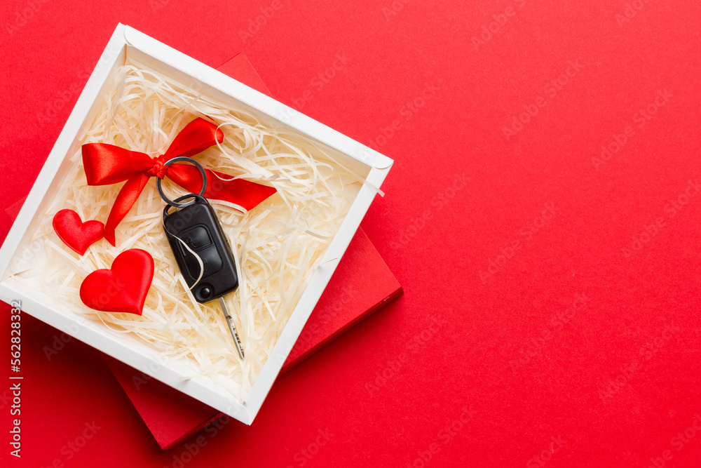 Black car key in a present box with a ribbon and red heart on colored background. Valentine day composition Top view - obrazy, fototapety, plakaty 