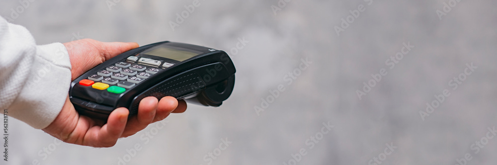 Payment terminal for cashless payments in hand. Paying with a credit card. Long banner. Payment terminal for cashless payments in hand. Paying with a credit card. Long banner.