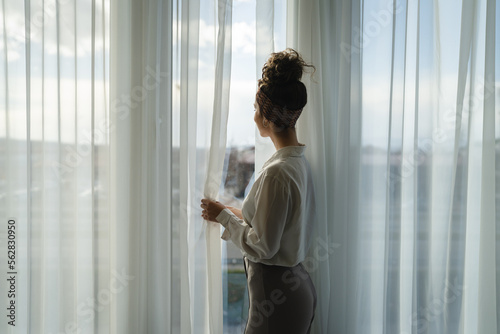 One woman beautiful caucasian stand by the window at home or hotel